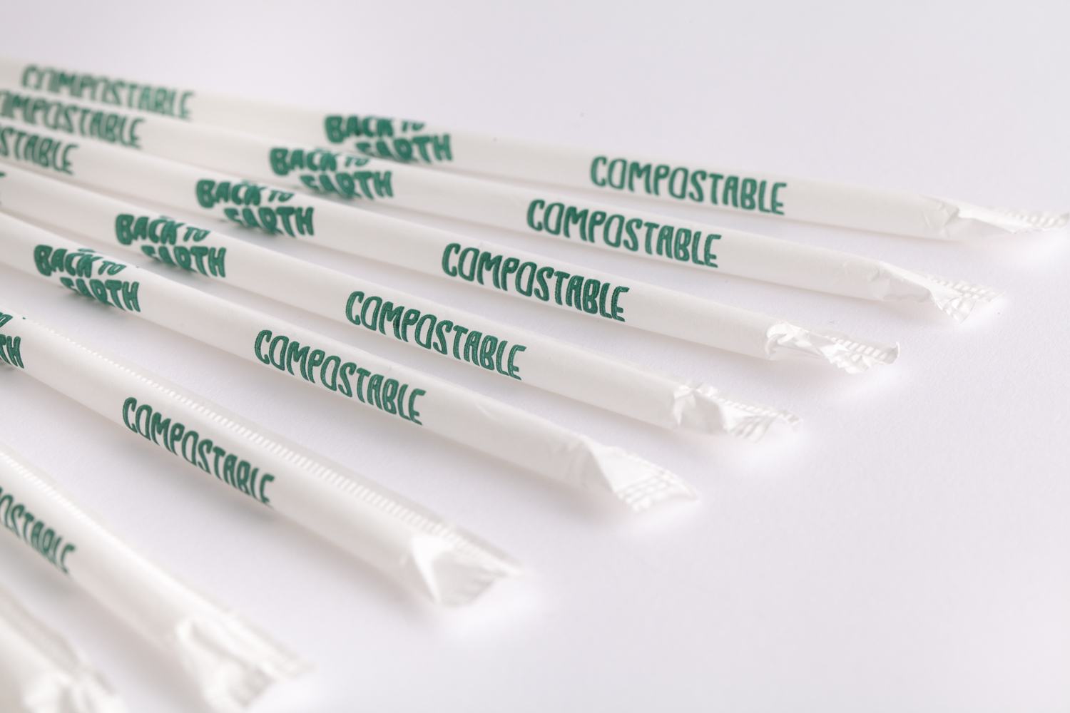 close up line of straws with white paper covers that say "Back to Earth" as well as "compostable" on them