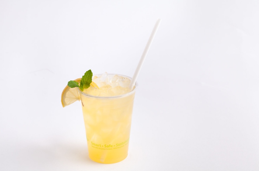 Plastic cup with lemon juice, garnished with lemon and mint. Served with a white paper straw.