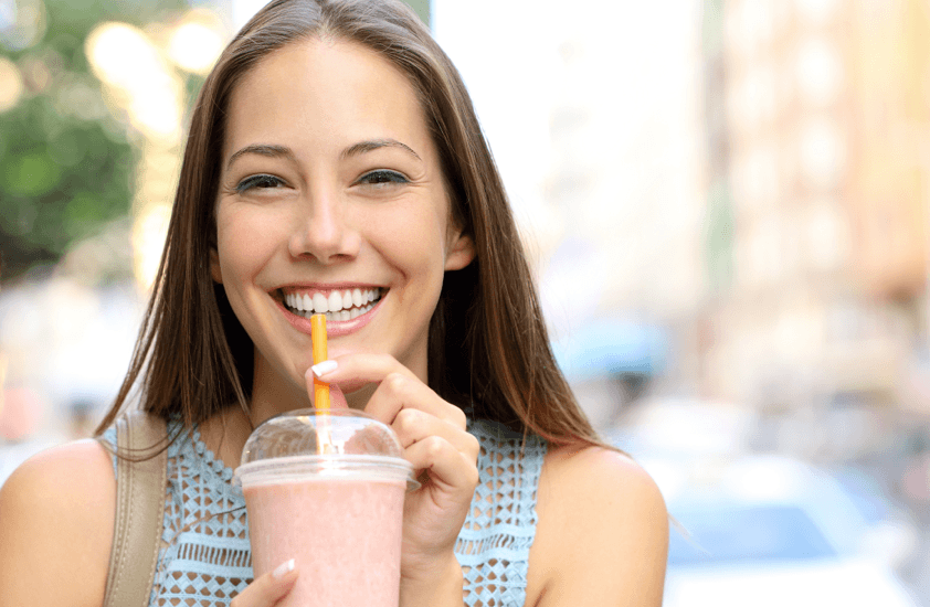 woman smiling enjoying drinking smoothie from clear cup with yellow compostable straw