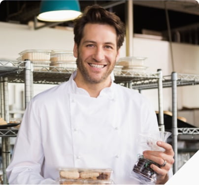 chef holding baked goods and smiling in front of cooling racks