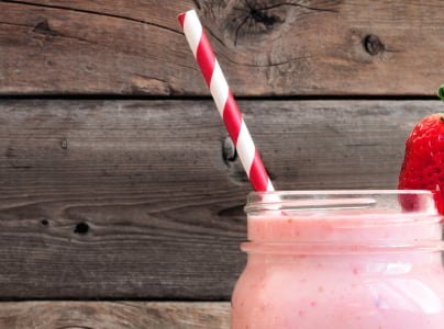zoomed in view of glass cup with strawberry smoothie and rainbow straw