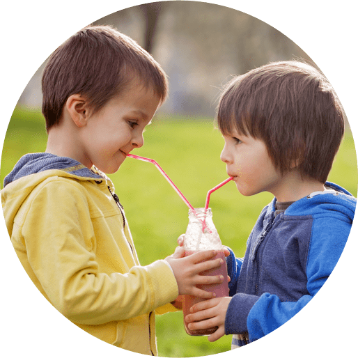 two young boys each sipping out of straws leading to the same jar