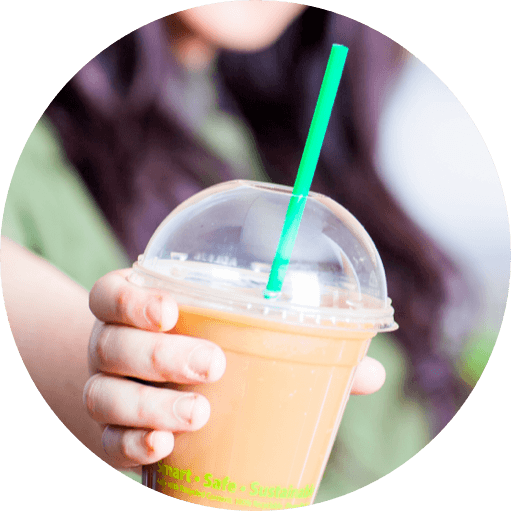 person holding up smoothie in clear cup with lid and green straw