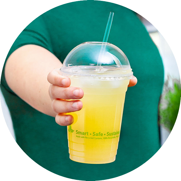person holding up juice drink in clear cup with lid and straw